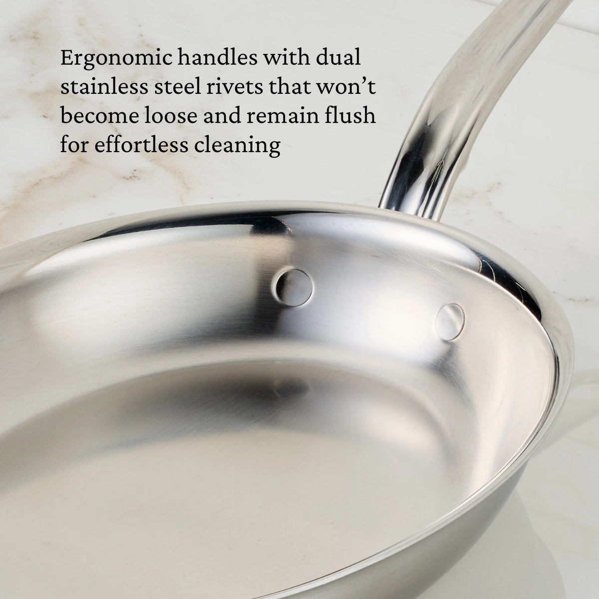 The Hestan Provisions Oval Fish Pan, made of stainless steel with a curved handle and dual rivets, sits elegantly on a light marble surface. Its ergonomic handles ensure even heat distribution and remain flush for easy cleaning.