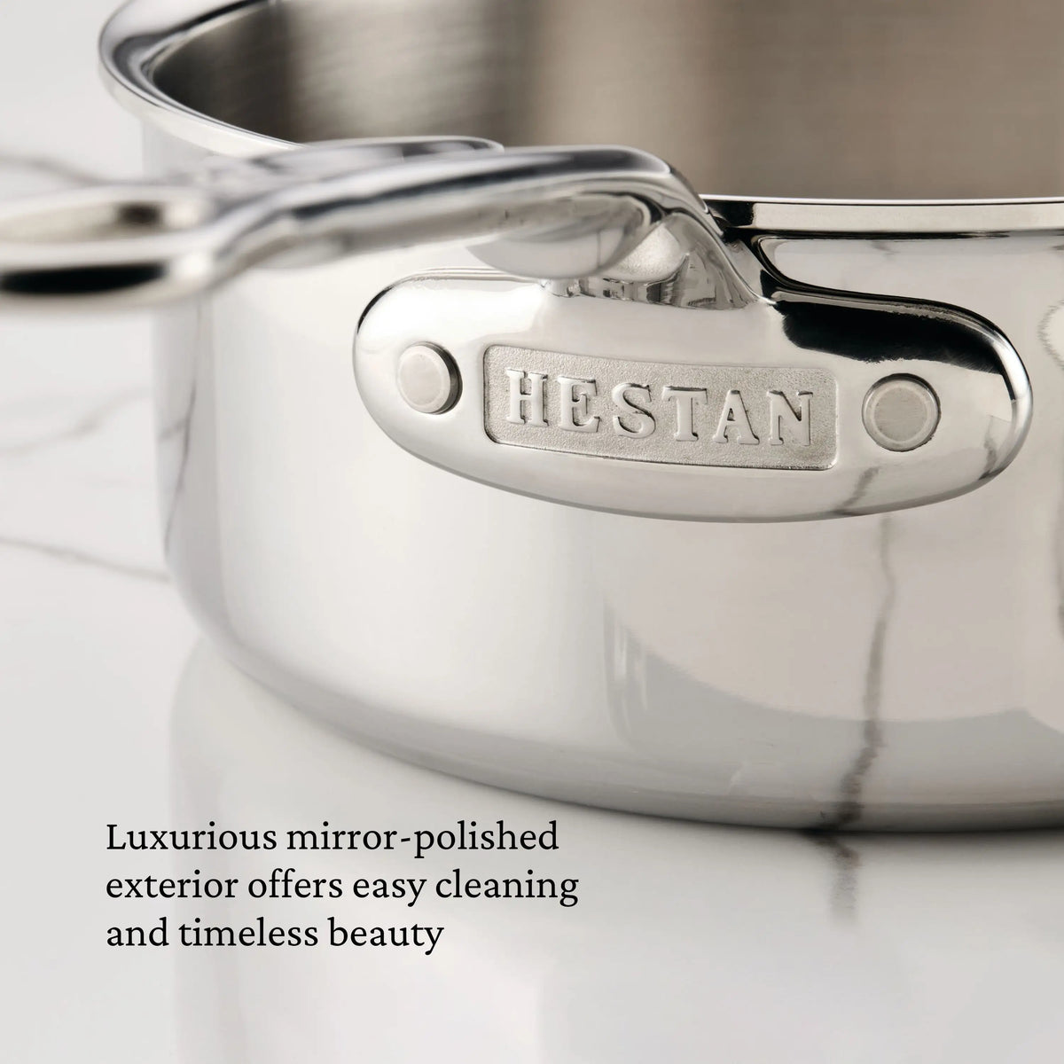 A close-up of a ProBond® Luxe™ Polished Clad Stainless Steel Saucepan with Lid sits on white marble. Text reads: “Luxurious mirror-polished exterior offers easy cleaning and timeless beauty.”.