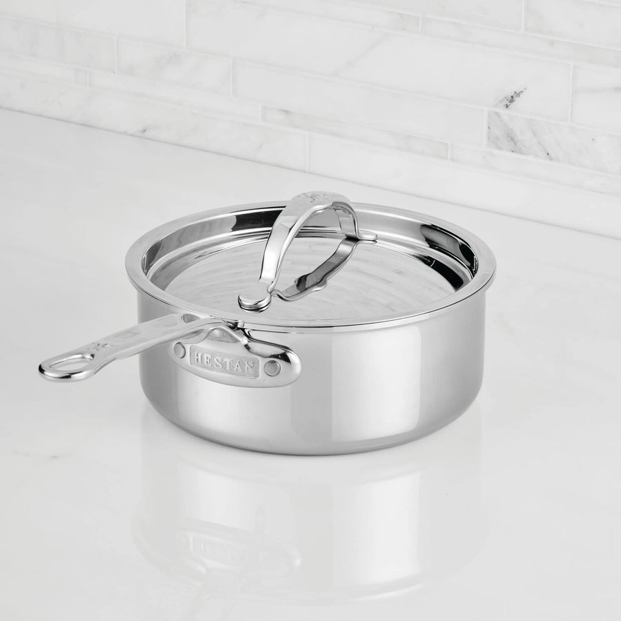 A ProBond® Luxe™ Polished Clad Stainless Steel Saucepan with Lid rests on a white countertop before a white tile backsplash, its handle engraved with the brand name.