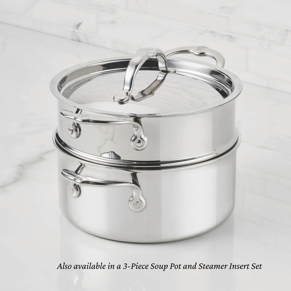 A ProBond® Luxe™ Professional Clad Stainless Steel Soup Pot with Lid sits on a matching steamer insert, both with metal handles, on a white marble countertop. Also available as a 3-piece Soup Pot and Steamer Insert Set.