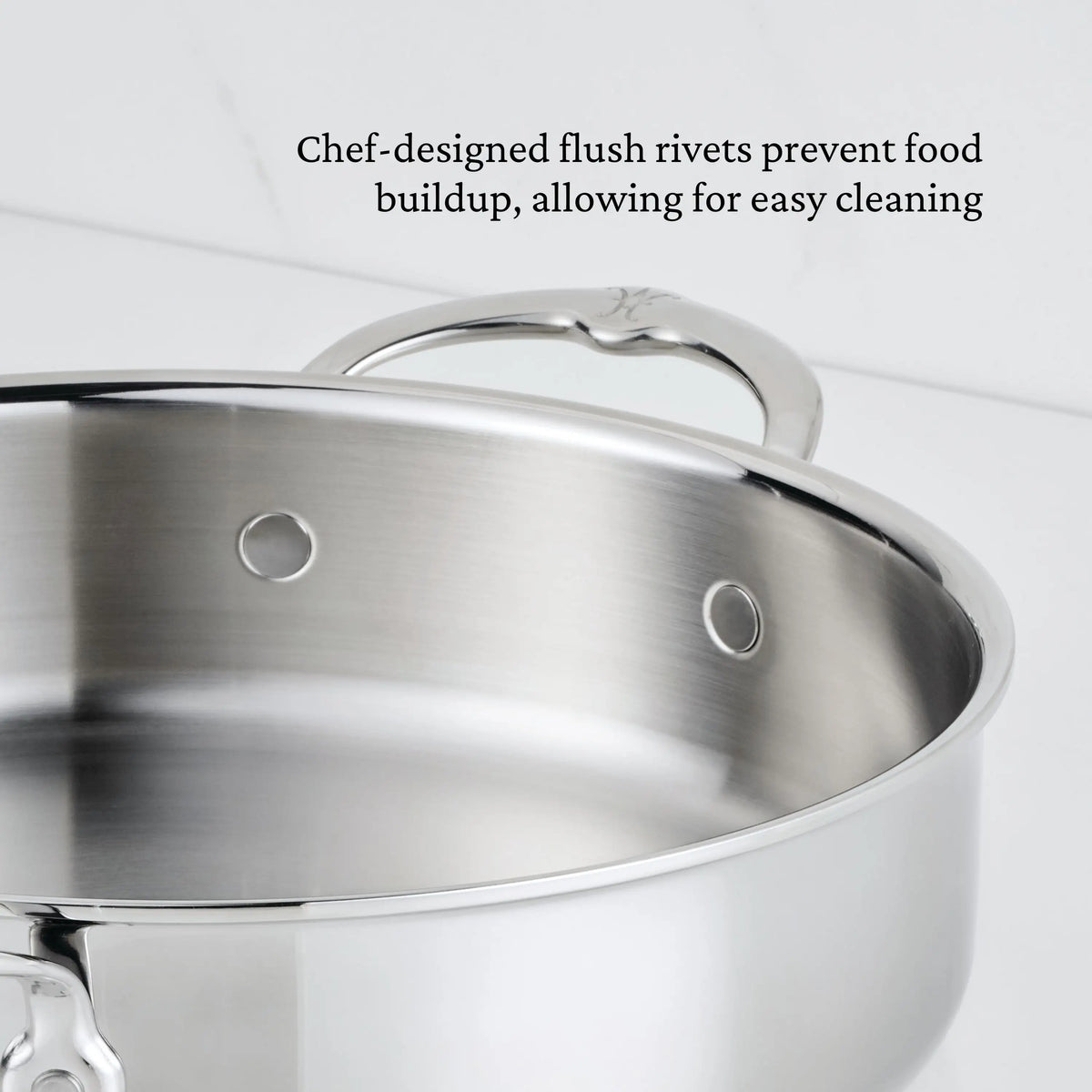 A close-up of the ProBond® Luxe™ Polished Clad Stainless Steel Braiser with Lid, 3.5-Quart, shows flush rivets and a handle on a white surface. Text reads: “Chef-designed flush rivets prevent food buildup for easy cleaning.”.