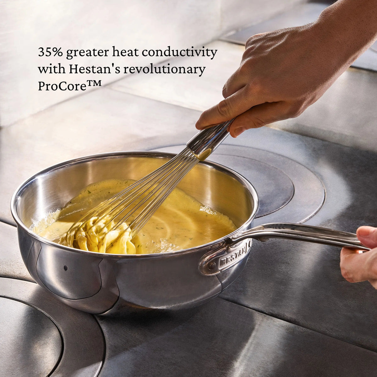 A person whisks a creamy yellow mixture in a ProBond® Luxe™ Professional Clad Stainless Steel Essential Pan on the stove. Text: “ProCore™ delivers 35% greater heat conductivity—enjoy professional results with ProBond® Luxe™ cookware.”.