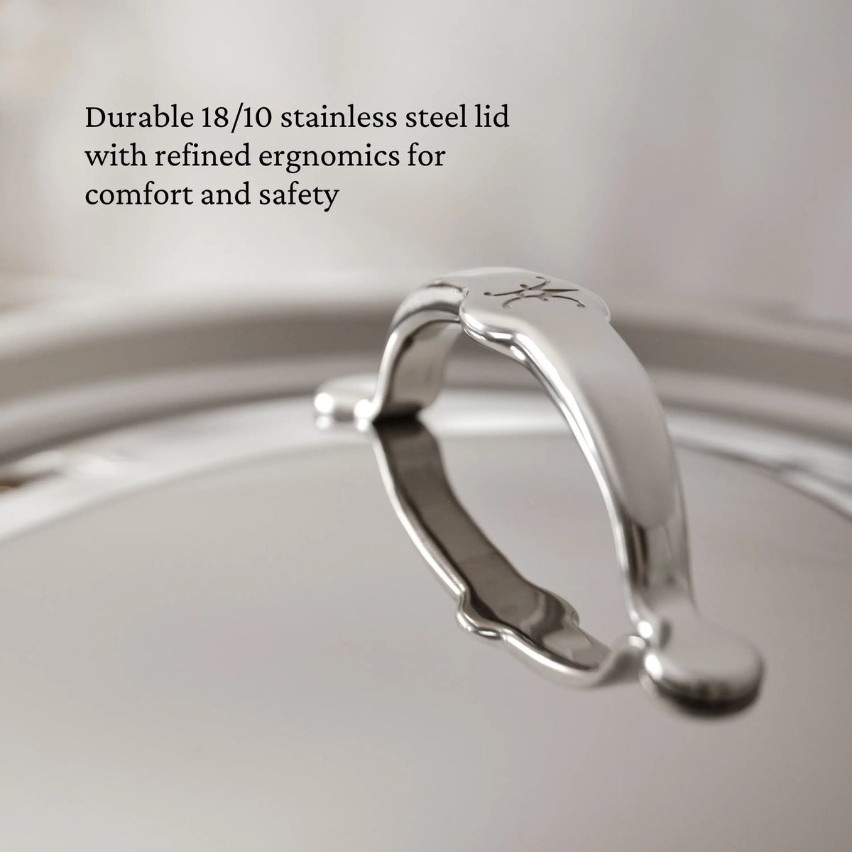 Close-up of a ProBond® Luxe™ Professional Clad Stainless Steel Essential Pan lid, featuring a curved handle and engraved logo, showcases Italian craftsmanship, durability, and an ergonomic design for comfort and safety.