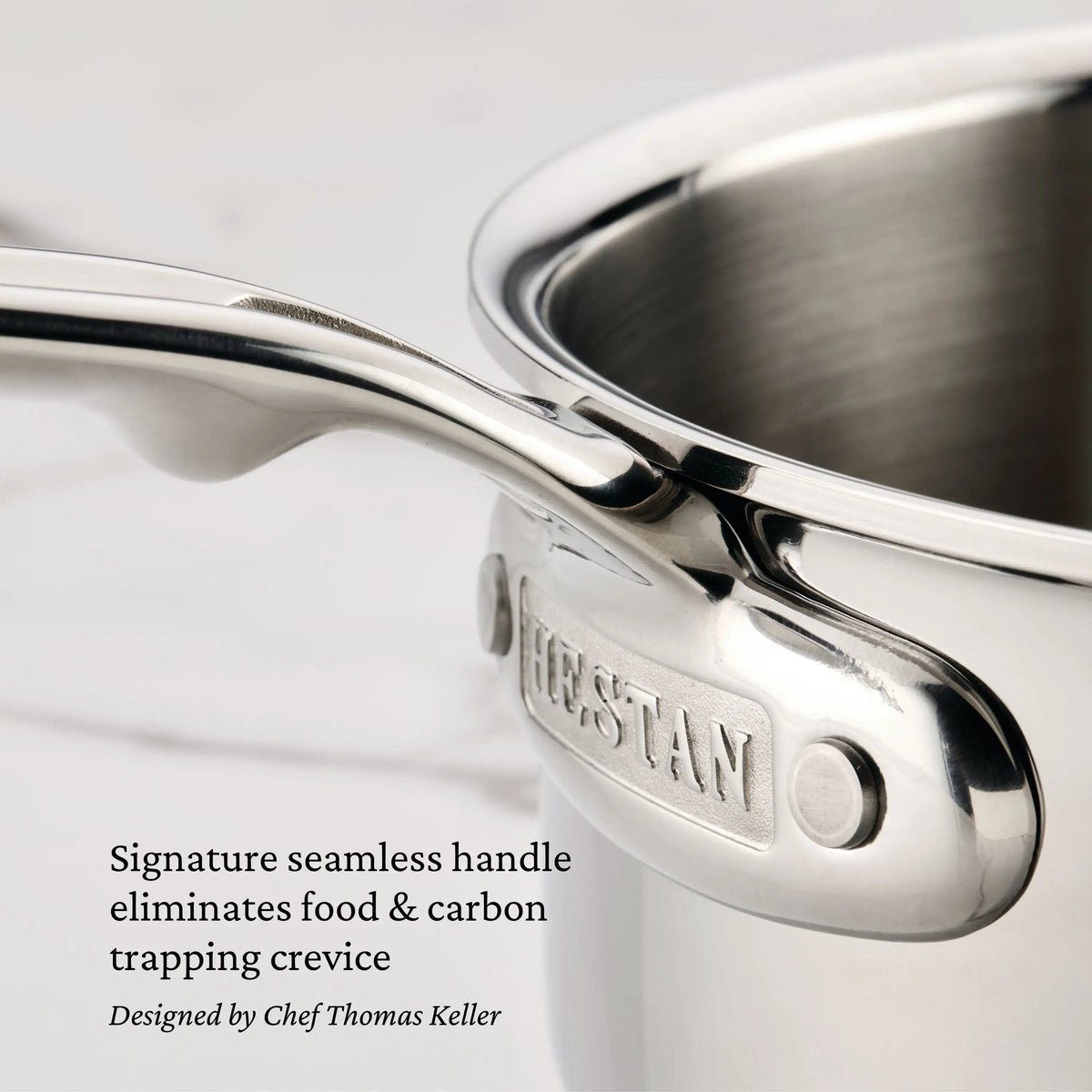 Close-up of a ProBond® Luxe™ Professional Clad Stainless Steel Essential Pan with Lid, featuring a seamless handle and “Hestan” engraved plate. Text highlights Italian craftsmanship and a design that resists food trapping.