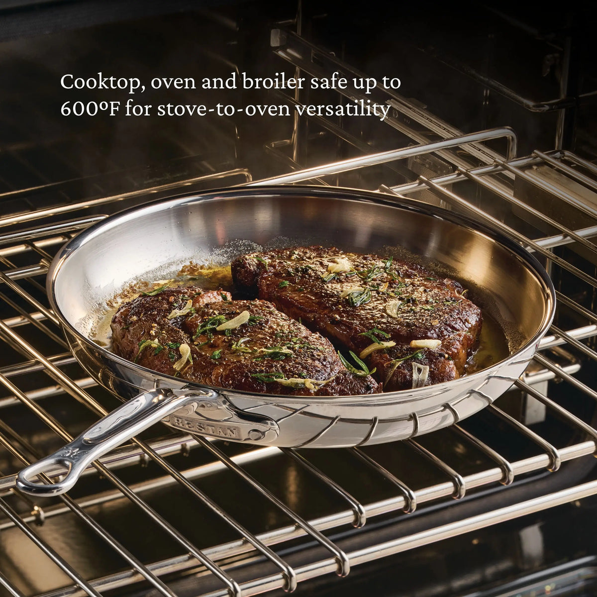 A ProBond® Luxe™ Polished Clad Stainless Steel Skillet with two seared steaks rests on an oven rack, demonstrating its versatility—its safe for cooktop, oven, and broiler use up to 600°F.