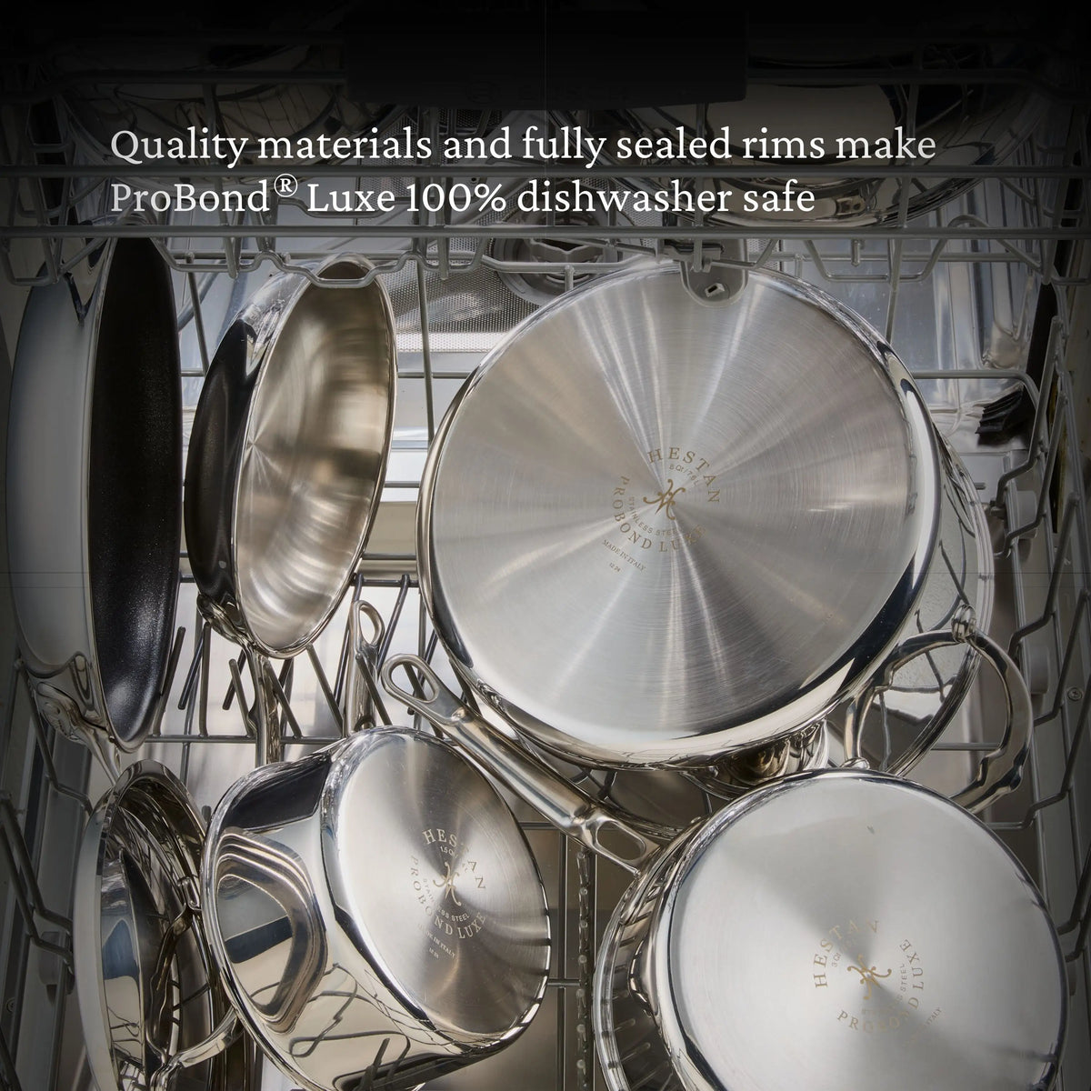 Several stainless steel pots and pans, including the ProBond® Luxe™ Polished Clad Stainless Steel Wok with Dome Lid, 14-Inch, are arranged in a dishwasher. A text overlay reads: “Quality materials and sealed rims make ProBond Luxe 100% dishwasher safe.”.