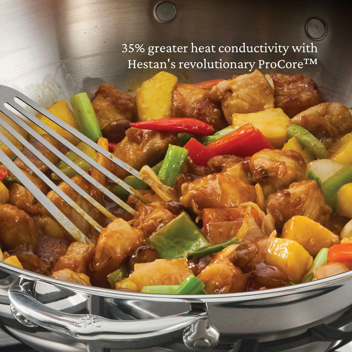 A ProBond® Luxe™ Polished Clad Stainless Steel Wok with Dome Lid, 14-Inch, and a metal spatula stir chicken, green onions, bell peppers, pineapple, and sauce. Text above highlights heat conductivity and Hestan ProCore aluminum core technology.