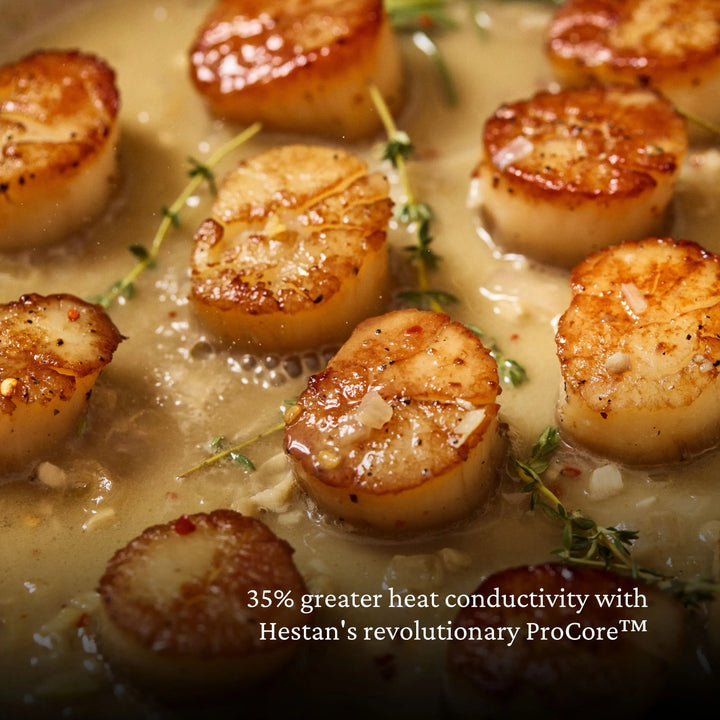 Scallops sizzle in a pan with sauce and herbs. Text reads: ProBond® Luxe™ Polished Clad Stainless Steel Skillets with TITUM® Nonstick offer 35% greater heat conductivity thanks to revolutionary ProCore™ technology.