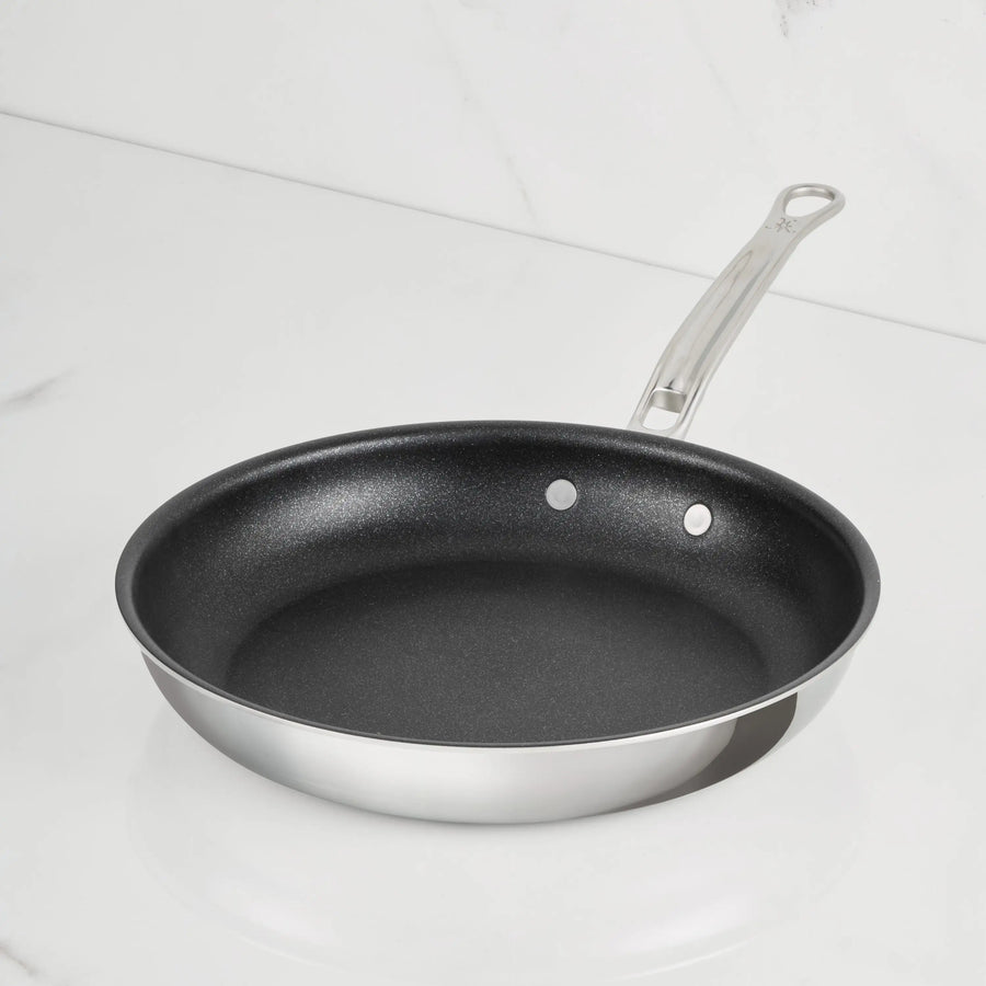 A ProBond Luxe® Polished Clad Stainless Steel Skillet with TITUM® Nonstick black interior and a metal handle, highlighting Italian craftsmanship, sits on a white marble countertop.