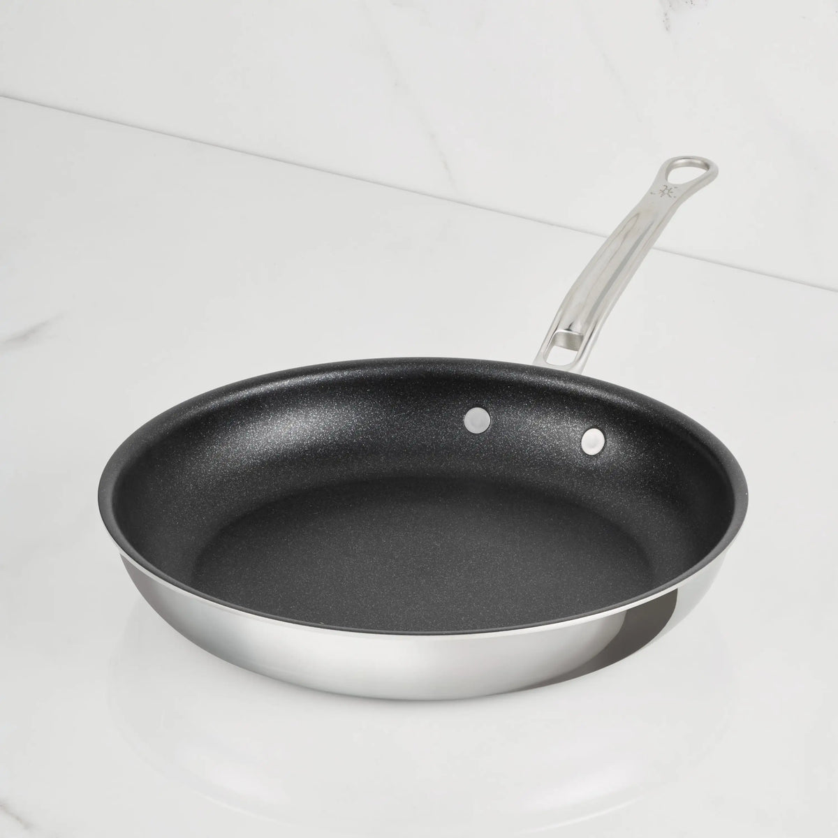 A ProBond Luxe® Polished Clad Stainless Steel Skillet with TITUM® Nonstick black interior and a metal handle, highlighting Italian craftsmanship, sits on a white marble countertop.