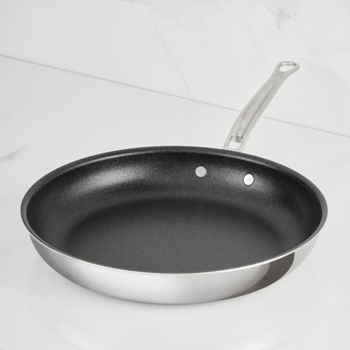 A ProBond Luxe® Polished Clad Stainless Steel Skillet with a TITUM® Nonstick interior and a metal handle sits on a white, marble-like countertop.