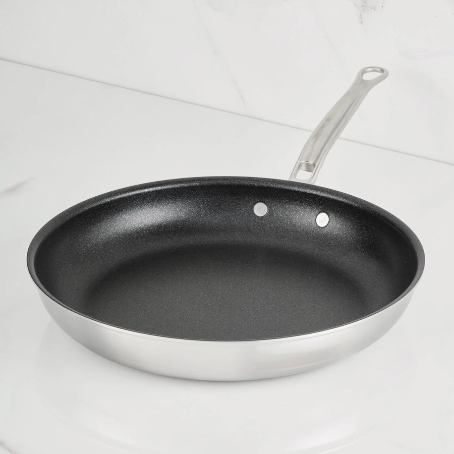 A ProBond® Luxe™ Polished Clad Stainless Steel Skillet with TITUM® Nonstick and a metal handle sits on a white marble countertop with a matching backsplash.