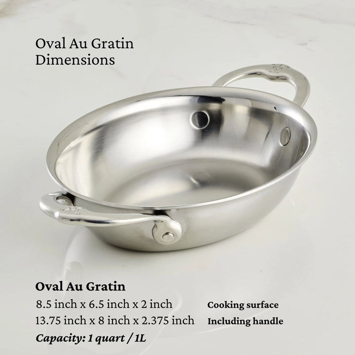 The Hestan Provisions 8.5-Inch x 6.5-Inch Oval Au Gratin pan, made of stainless steel and featuring two handles, is displayed on a light countertop. It holds 1 quart (1L) and measures 8.5"x6.5"x2" including handles.