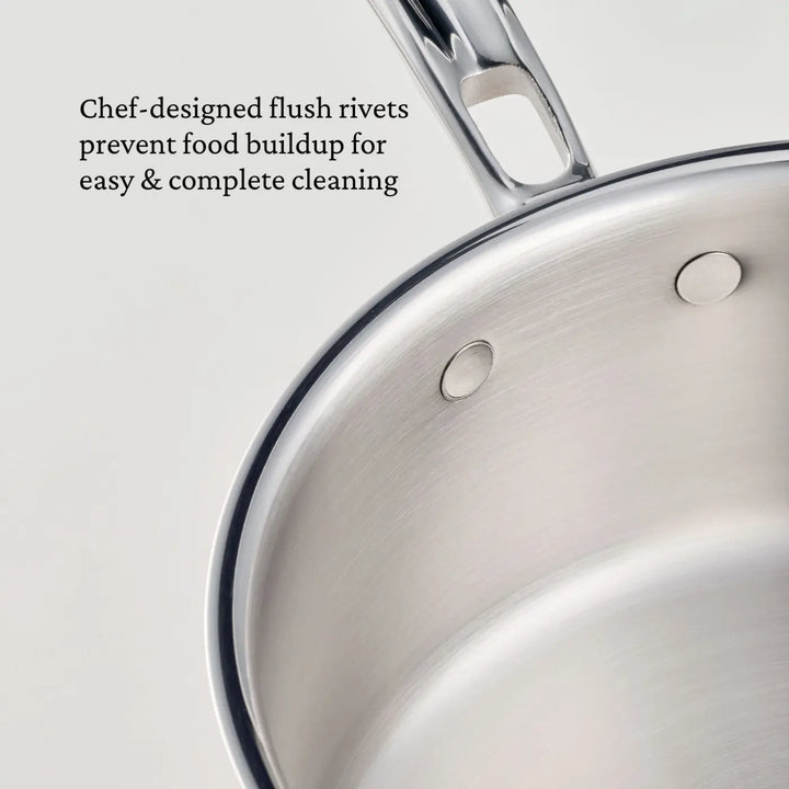 Close-up of a stainless steel saucepan from the CopperBond® Aura™ Polished Copper 10-Piece Cookware Set, featuring smooth, flush rivets that securely attach the handle. Text on the image reads: Chef-designed flush rivets prevent food buildup for easy & thorough cleaning.