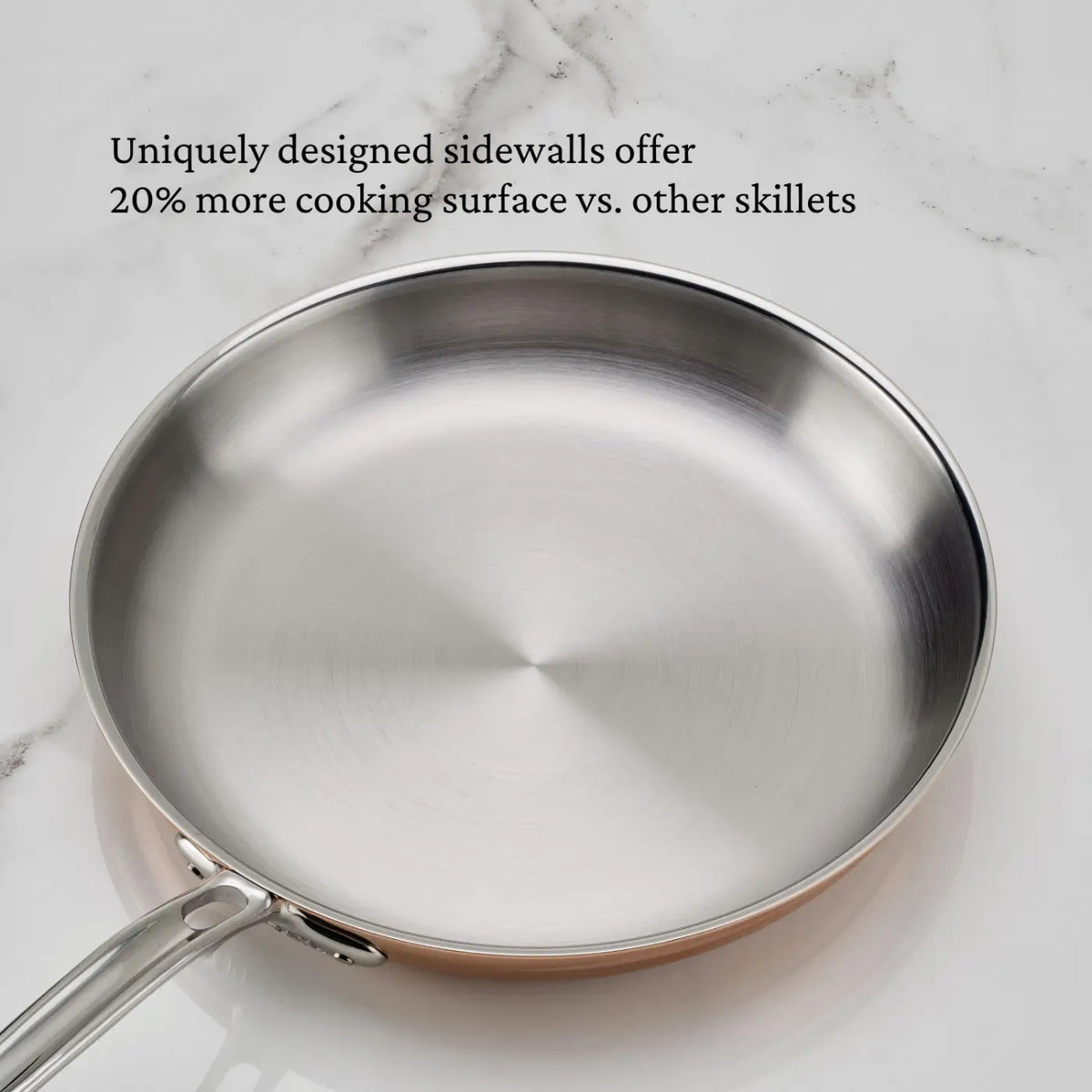A CopperBond® Aura™ Polished Copper 10-Piece Cookware Set skillet with a wide, flat cooking surface rests on a white marble countertop. Text above the pan reads: “Uniquely designed sidewalls offer 20% more cooking surface vs. other skillets.” Ideal for any copper kitchen, this professional-grade set blends superior performance with timeless style.