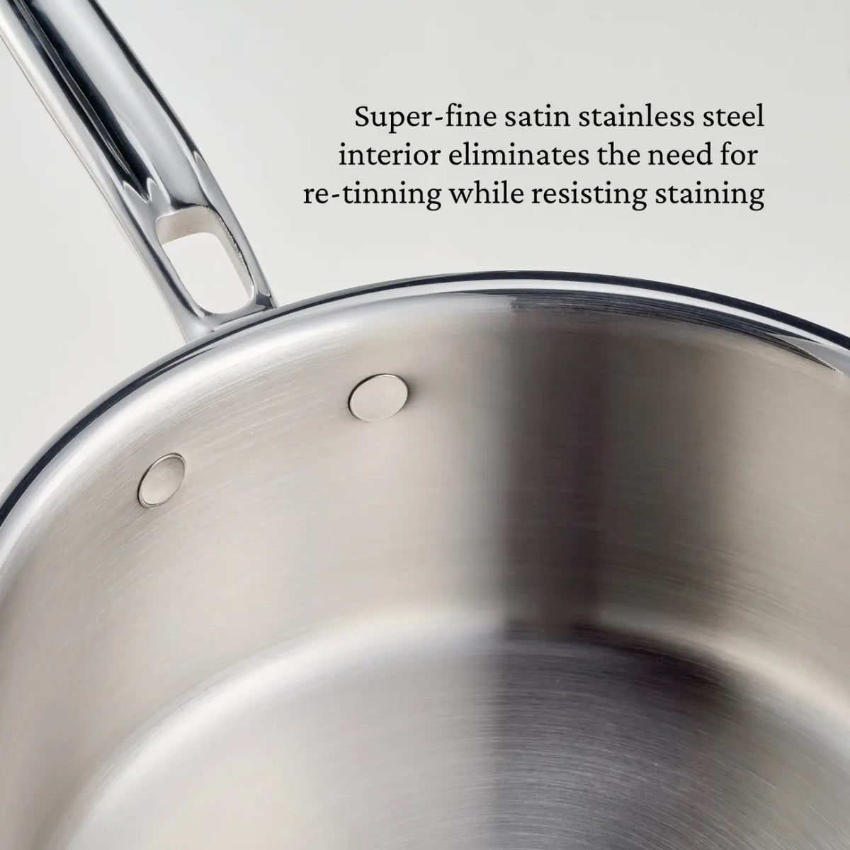 A close-up of the CopperBond® Aura™ Polished Copper Saucepans with Lid highlights its stainless steel interior, which resists staining and eliminates the need for re-tinning. The partially visible handle displays a sleek, modern design characteristic of high-quality copper cookware. The pan features a satin finish that enhances its contemporary appearance.