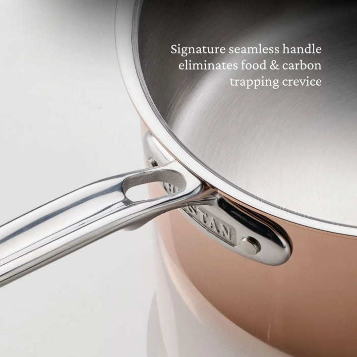 A close-up of a CopperBond® Aura™ Polished Copper Saucepan with a seamless metal handle, securely attached to the polished copper-colored pot. Text reads: Signature seamless handle eliminates food & carbon trapping crevice. The premium copper cookware features a stainless steel interior for optimum performance and durability.