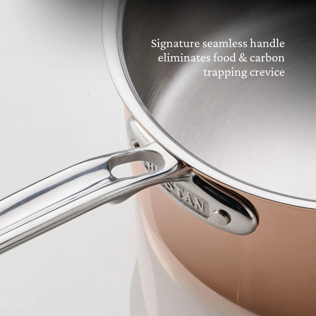 A close-up of a CopperBond® Aura™ Polished Copper Saucepan with a seamless metal handle, securely attached to the polished copper-colored pot. Text reads: Signature seamless handle eliminates food & carbon trapping crevice. The premium copper cookware features a stainless steel interior for optimum performance and durability.