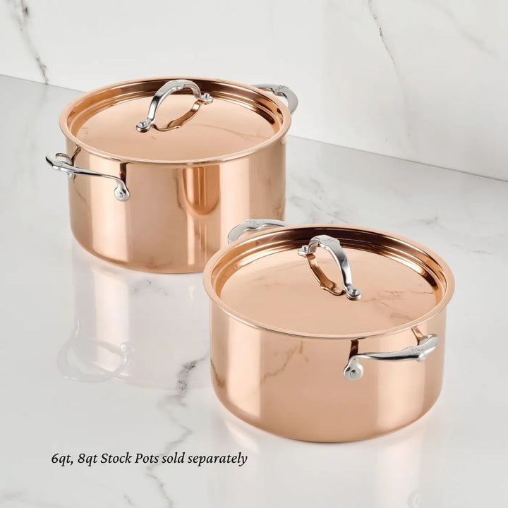 Two polished CopperBond® Aura™ stock pots with lids and sturdy metal handles are displayed on a white marble surface. Part of the premium Polished Copper Stock Pots with Lid collection, these pots feature a durable stainless steel interior for superior heat conduction and easy cleaning. Shown side by side in 6-quart and 8-quart sizes, each pot is sold separately.