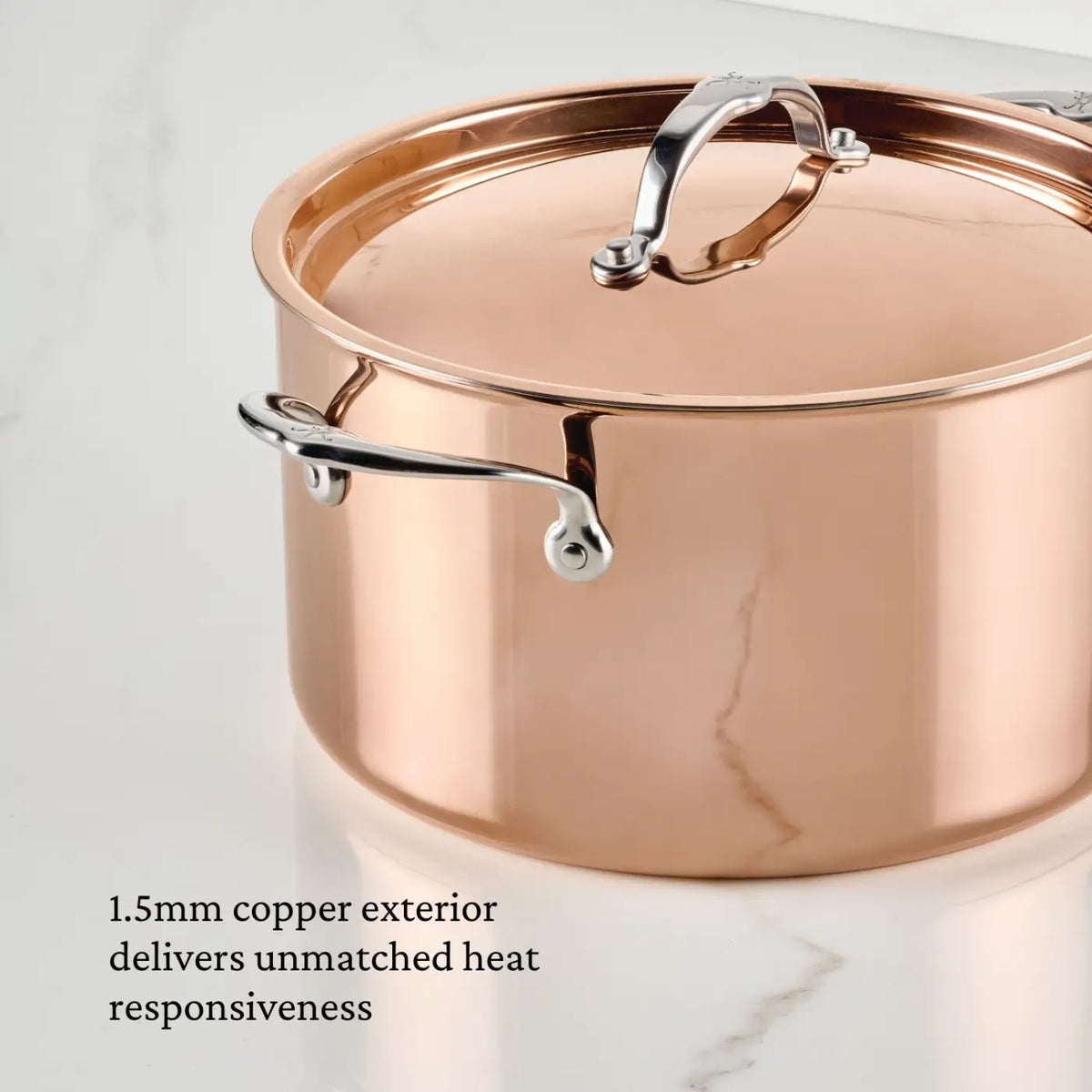 A CopperBond® Aura™ Polished Copper Stock Pot with Lid and stainless steel handles rests on a marble surface. The text reads, “1.5mm copper exterior delivers unmatched heat responsiveness—an essential feature of premium copper cookware.”.