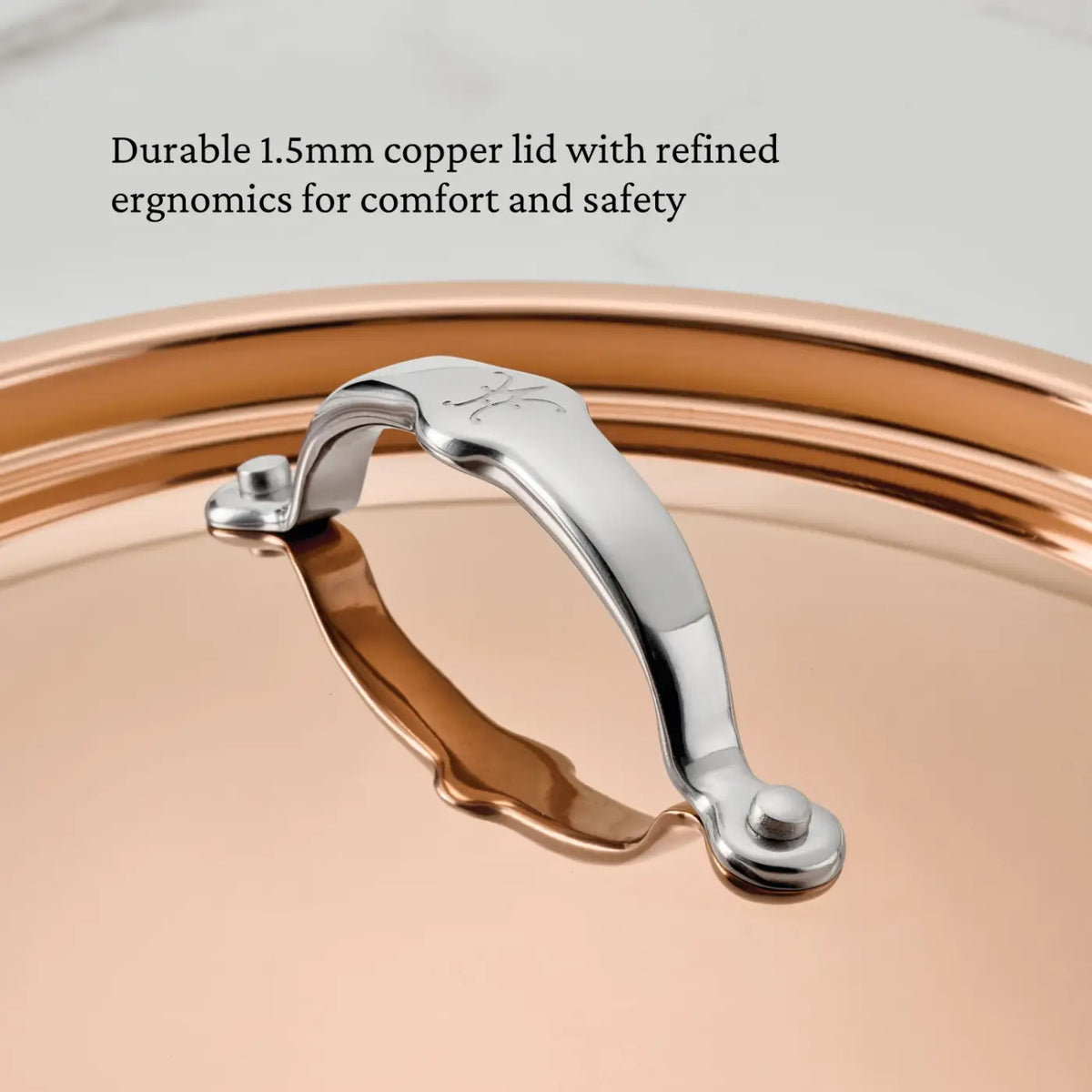 Close-up of a shiny stainless steel handle affixed to the lid of CopperBond® Aura™ Polished Copper Essential Pans. Black text above reads: Durable 1.5mm copper lid with refined ergonomics for comfort and safety, inspired by Italian crafted cookware.
