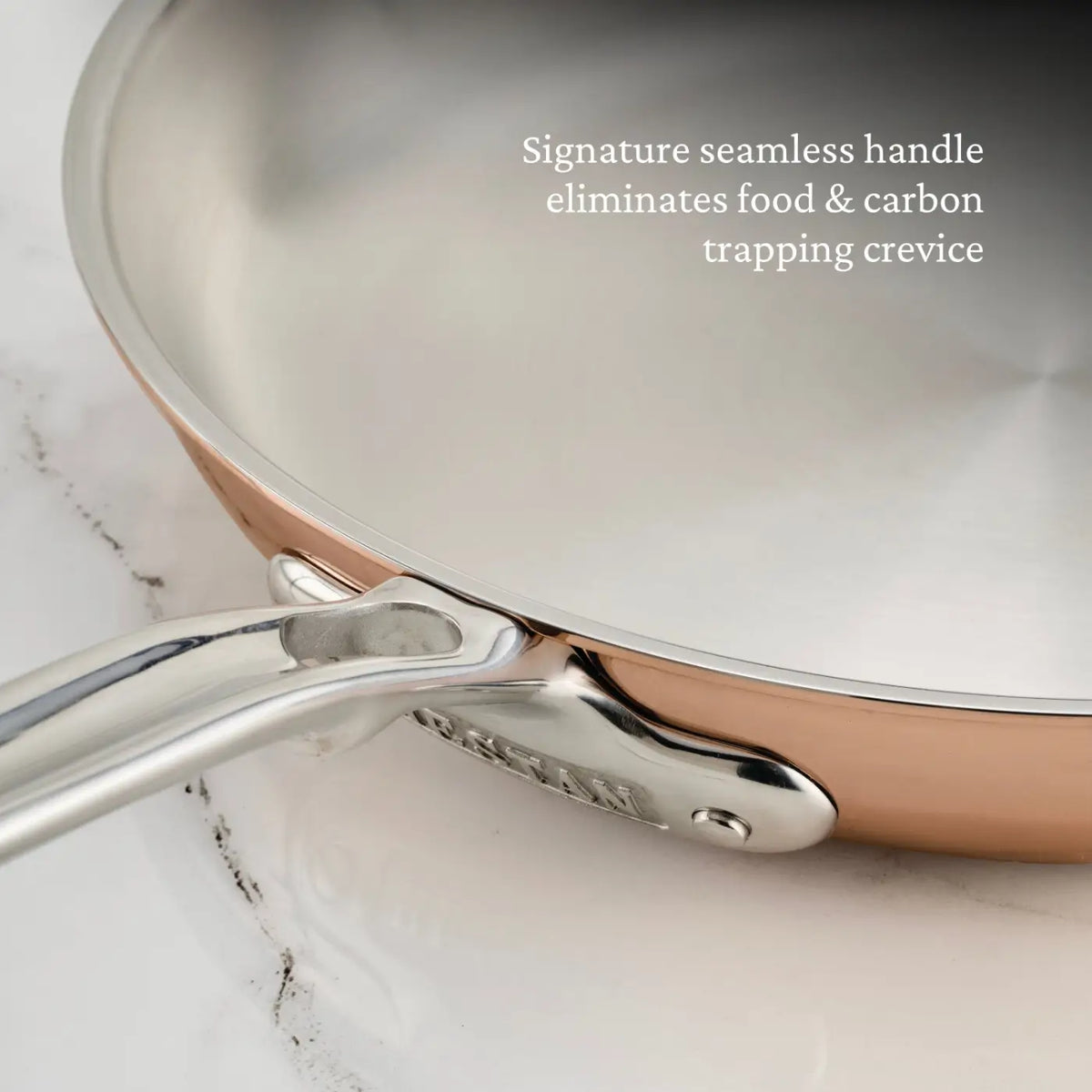 Close-up of a CopperBond® Aura™ Polished Copper Skillet, featuring a copper exterior and stainless steel interior with a seamless handle attachment. Text on the image reads: Signature seamless handle eliminates food & carbon trapping crevice, elevating Polished Copper Skillets to new heights of professional performance.