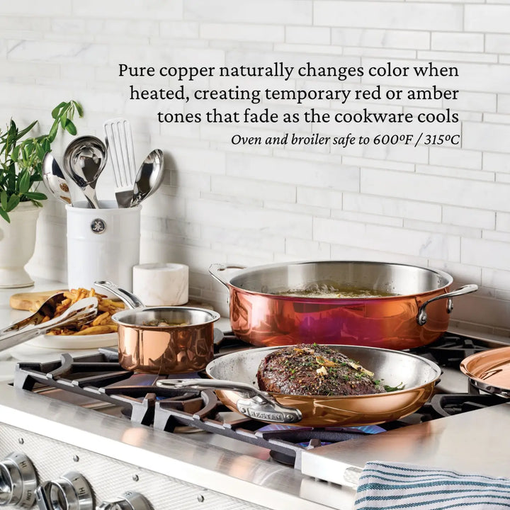 CopperBond® Aura™ Polished Copper Skillets sit on a stovetop, including a saucepan, a steak-searing skillet, and a sauté pan—all crafted with stainless steel interiors for enhanced durability. The professional-grade CopperBond® Aura™ cookware gleams beside kitchen utensils in a nearby holder. Above, text highlights copper’s color change with heat and the oven safety of these skillets.