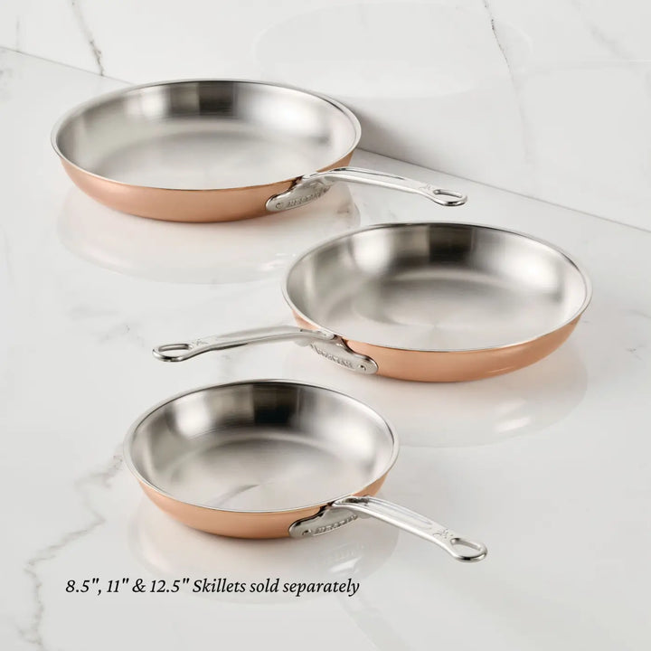 Three CopperBond® Aura™ Polished Copper Skillets, featuring stainless steel interiors and metal handles, are displayed on a white marble surface. Available in 8.5-, 11-, and 12.5-inch diameters, these professional-grade skillets are sold separately.