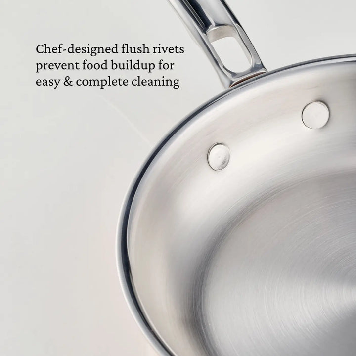 A close-up of a CopperBond® Aura™ Polished Copper Skillet shows flush rivets at the base of its handle. Black text beside the skillet reads, Chef-designed flush rivets prevent food buildup for easy & complete cleaning, making it an essential piece of professional-grade cookware.