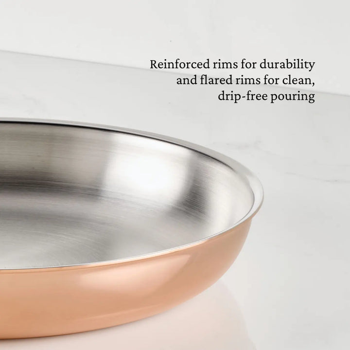 A close-up of a CopperBond® Aura™ Polished Copper Skillet with reinforced, flared rims sits on a white marble surface. Perfect for professional-grade cookware collections, the durable rims are designed for drip-free pouring, while the stainless steel interior ensures reliable performance.