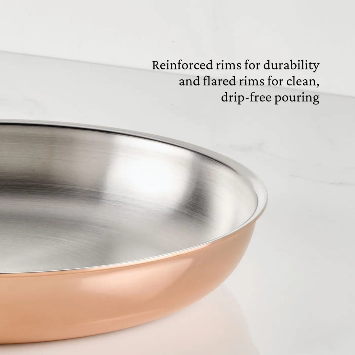A close-up of a CopperBond® Aura™ Polished Copper Skillet with reinforced, flared rims sits on a white marble surface. Perfect for professional-grade cookware collections, the durable rims are designed for drip-free pouring, while the stainless steel interior ensures reliable performance.