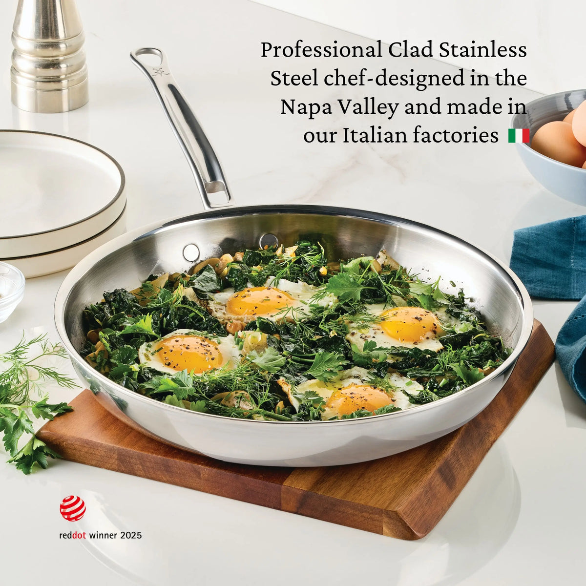 A ProBond® Luxe™ Polished Clad Stainless Steel Signature Skillet from the 7-Piece Set holds eggs, greens, and herbs on a board with eggs, a blue towel, pepper grinder, and herbs nearby. Text highlights its design and origin.