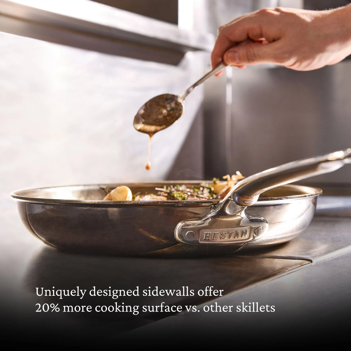 A hand drizzles sauce over food in a ProBond® Luxe™ Polished Clad Stainless Steel Signature Set, 7-Piece skillet on the stove. Text: Unique sidewalls provide 20% more cooking surface than other stainless steel cookware.