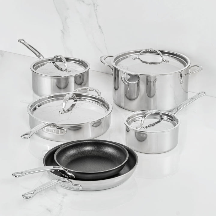 A ProBond Luxe® Polished Clad Stainless Steel 10-Piece Set, featuring four lidded pots and two black TITUM® nonstick frying pans, is elegantly arranged on a white marble countertop with a marbled white background—showcasing Italian craftsmanship at its finest.
