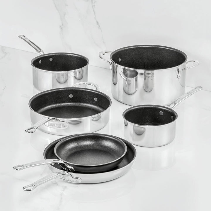 Inspired by Italian craftsmanship, the ProBond Luxe® Polished Clad Stainless Steel 10-Piece Set features TITUM® Nonstick interiors. This elegant collection includes two frying pans, two saucepans with handles, a sauté pan, and a large stock pot—all beautifully displayed on a white marble surface.