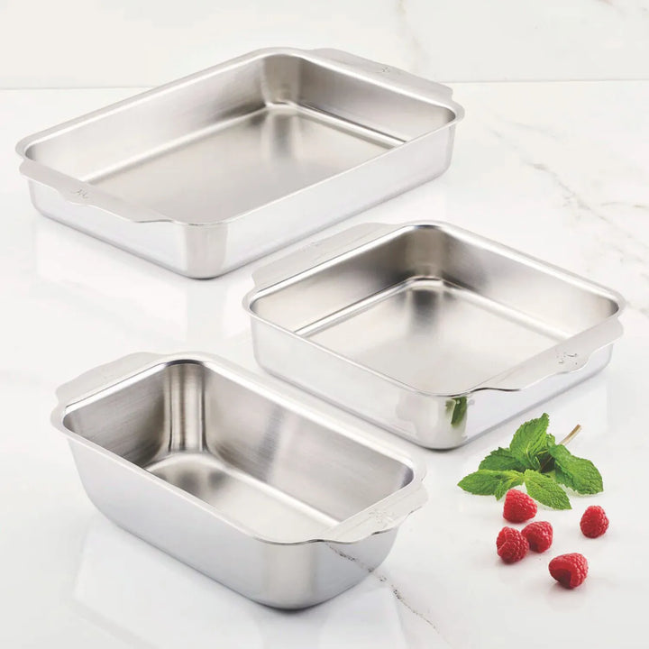 An OvenBond Tri-Ply 3-Piece Baking Set by Hestan Provisions sits on a marble surface, surrounded by fresh raspberries and green mint leaves. This warp-resistant stainless steel set ensures durability while adding elegance to your kitchen.