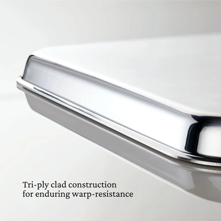 Close-up of a shiny Hestan OvenBond Tri-Ply Quarter Sheet Pan & Rack (9"x12") with smooth, reflective surfaces. Text reads: Tri-ply clad construction for lasting warp-resistance from the OvenBond Collection.