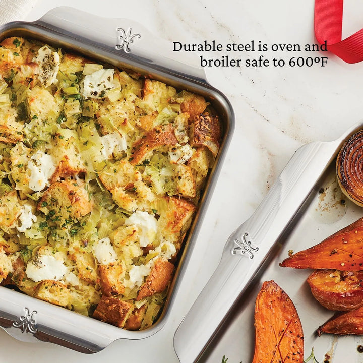 The Hestan Provisions™ OvenBond Tri-ply Square Baker, filled with stuffing made from bread cubes, herbs, and vegetables, rests near a tray with roasted sweet potatoes and a halved onion. This premium bake pan is warp-resistant and oven/broiler safe up to 600°F.