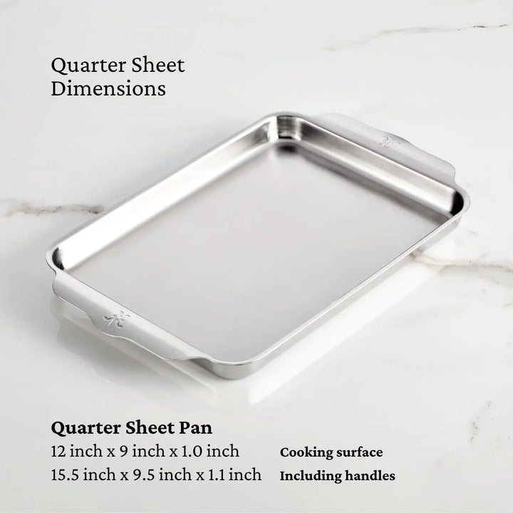 Image of a quarter sheet pan from the Hestan Provisions OvenBond Tri-ply 5-Piece Set on a marble surface. The shiny rectangular pan features handles and triple-bonded stainless steel, with dimensions of 12 x 9 x 1 inches for the cooking area and 15.5 x 9.5 x 1.1 inches overall.