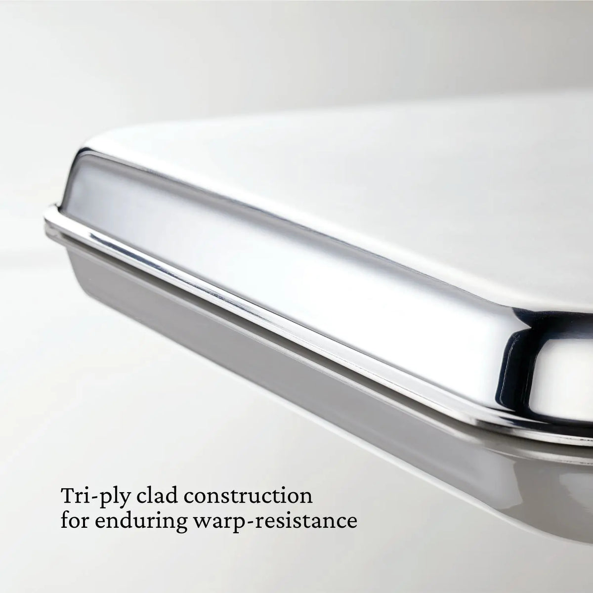 Close-up of OvenBond Tri-ply Medium Sheet Pan from Hestan Provisions, featuring a shiny rectangular stainless steel surface. The tri-ply clad construction ensures durability and warp resistance, making it oven safe at high temperatures, highlighted by clear text on the image.