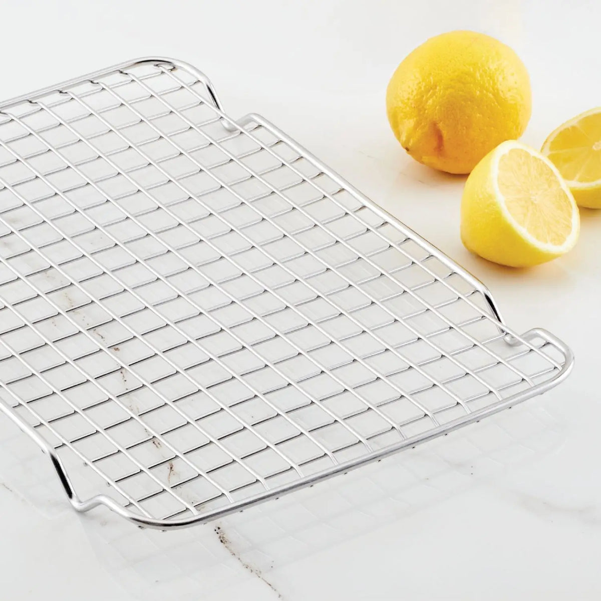 A Hestan Provisions OvenBond Stainless Steel Quarter Sheet Pan Rack elegantly rests on a white surface, accompanied by two whole lemons and a lemon half, gleaming with promise for its next culinary adventure.