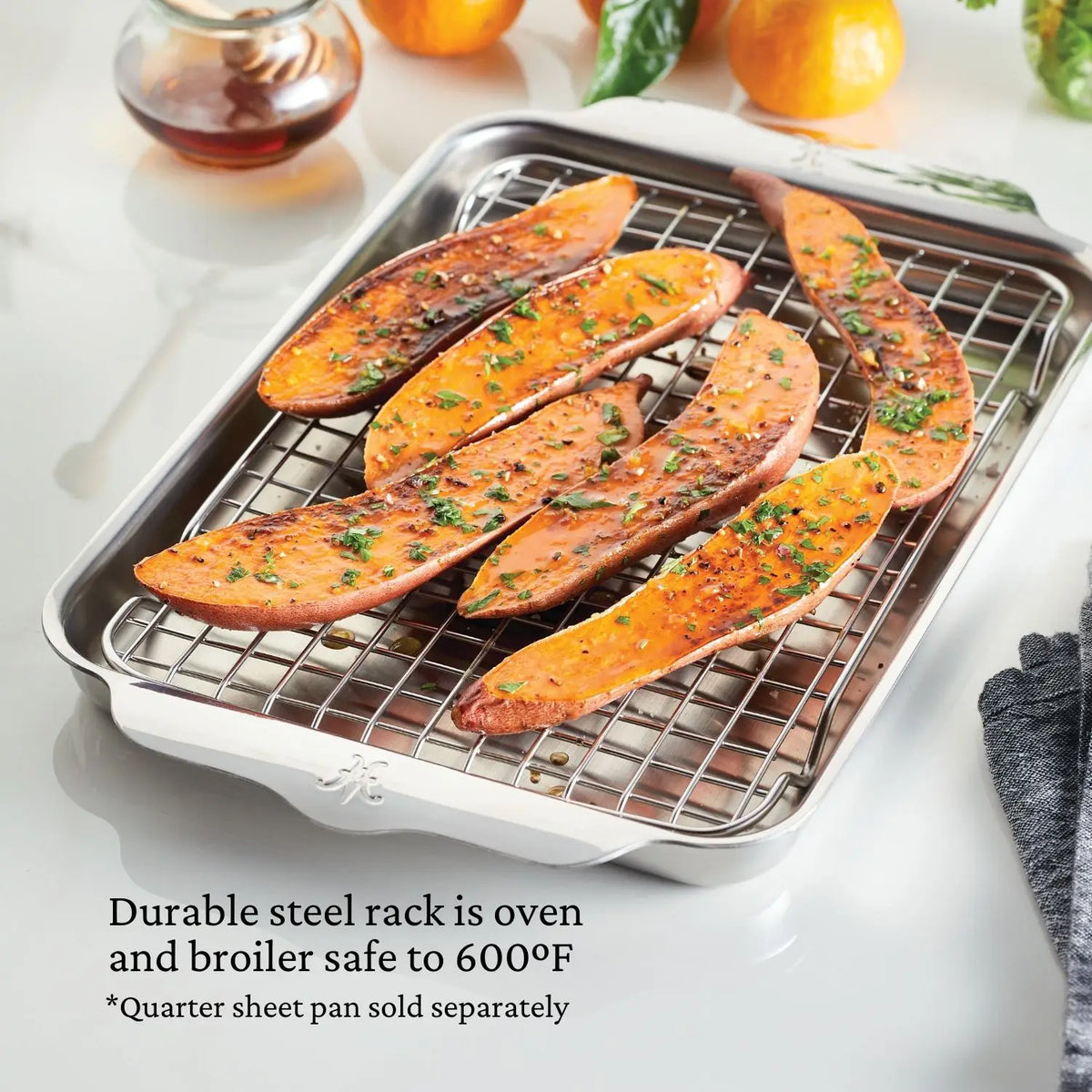 Seasoned sweet potato slices rest on a Hestan Provisions OvenBond Stainless Steel Quarter Sheet Pan Rack, known for durability and heat resistance up to 600°F, with a saucy dish visible in the background.