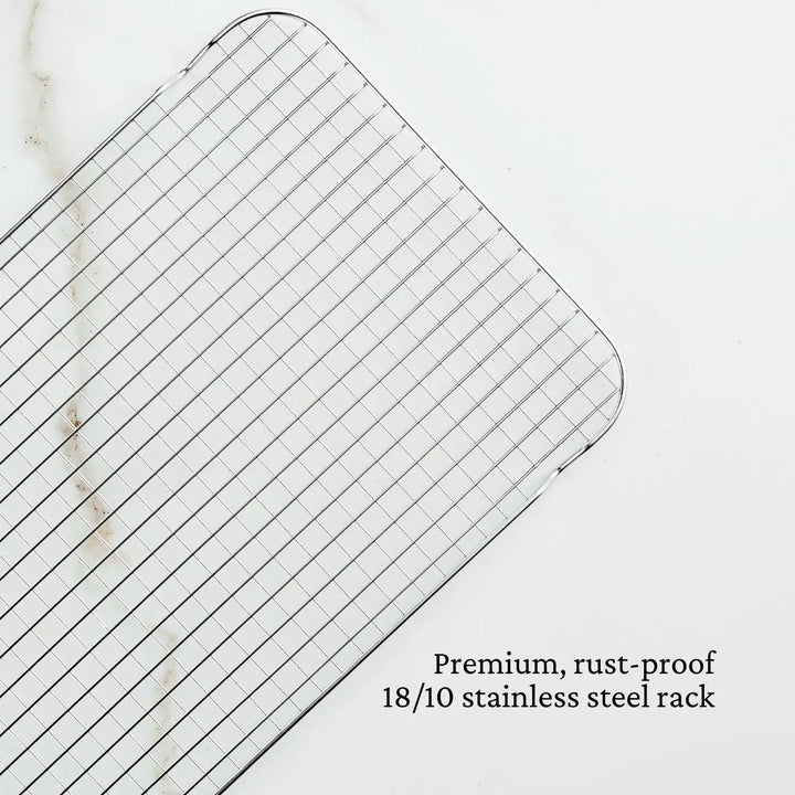 On a light marble surface lies a grid-patterned stainless steel cooling rack. The text says, Premium, rust-proof 18/10 stainless steel by Hestan Provisions, referring to the OvenBond Tri-ply 4-Piece Set.