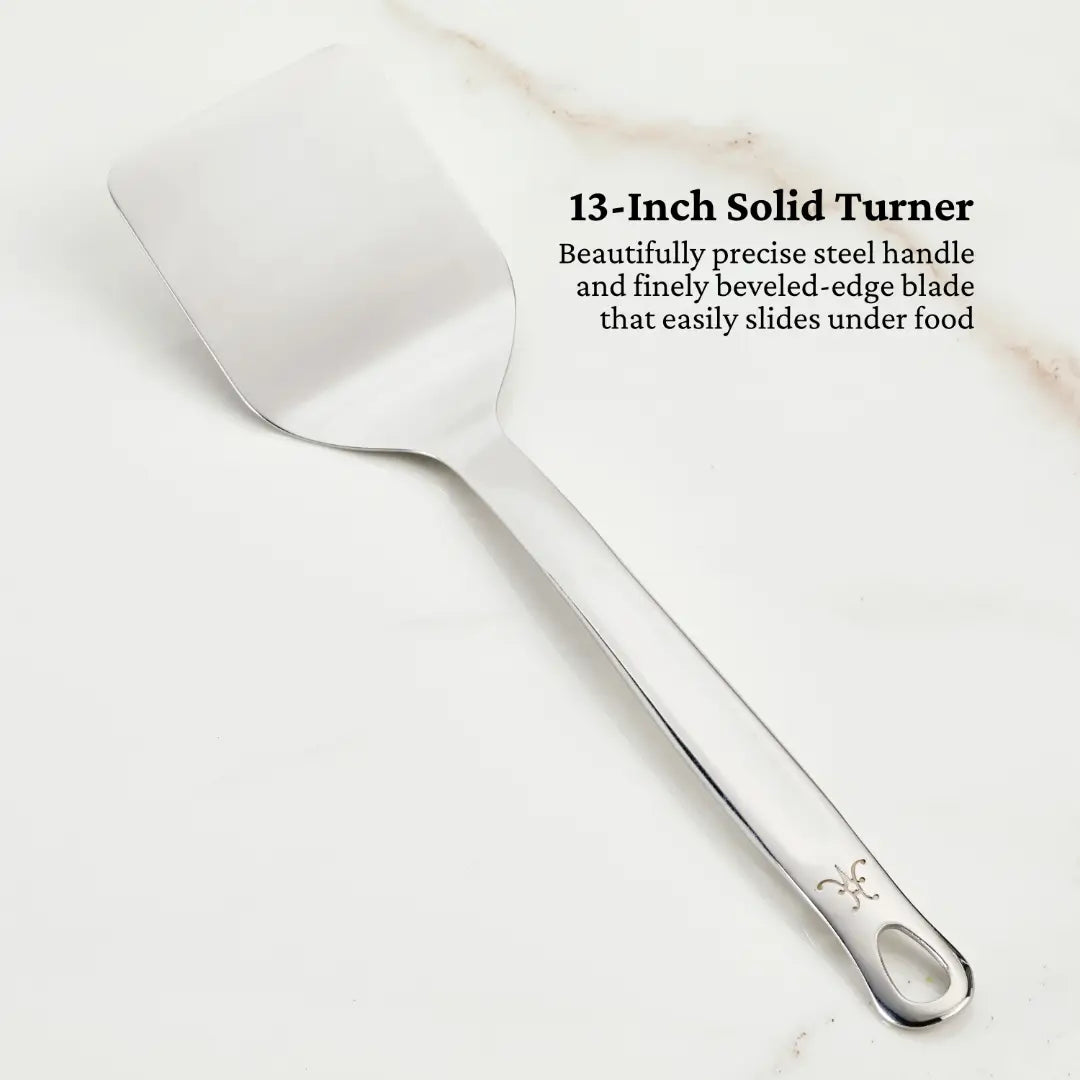 A 13-Inch Solid Turner from Hestan Provisions, featuring a finely beveled-edge blade and a precise steel handle, is displayed against a light background. Text reads: Essential Chefs Tool Set, 5-piece.