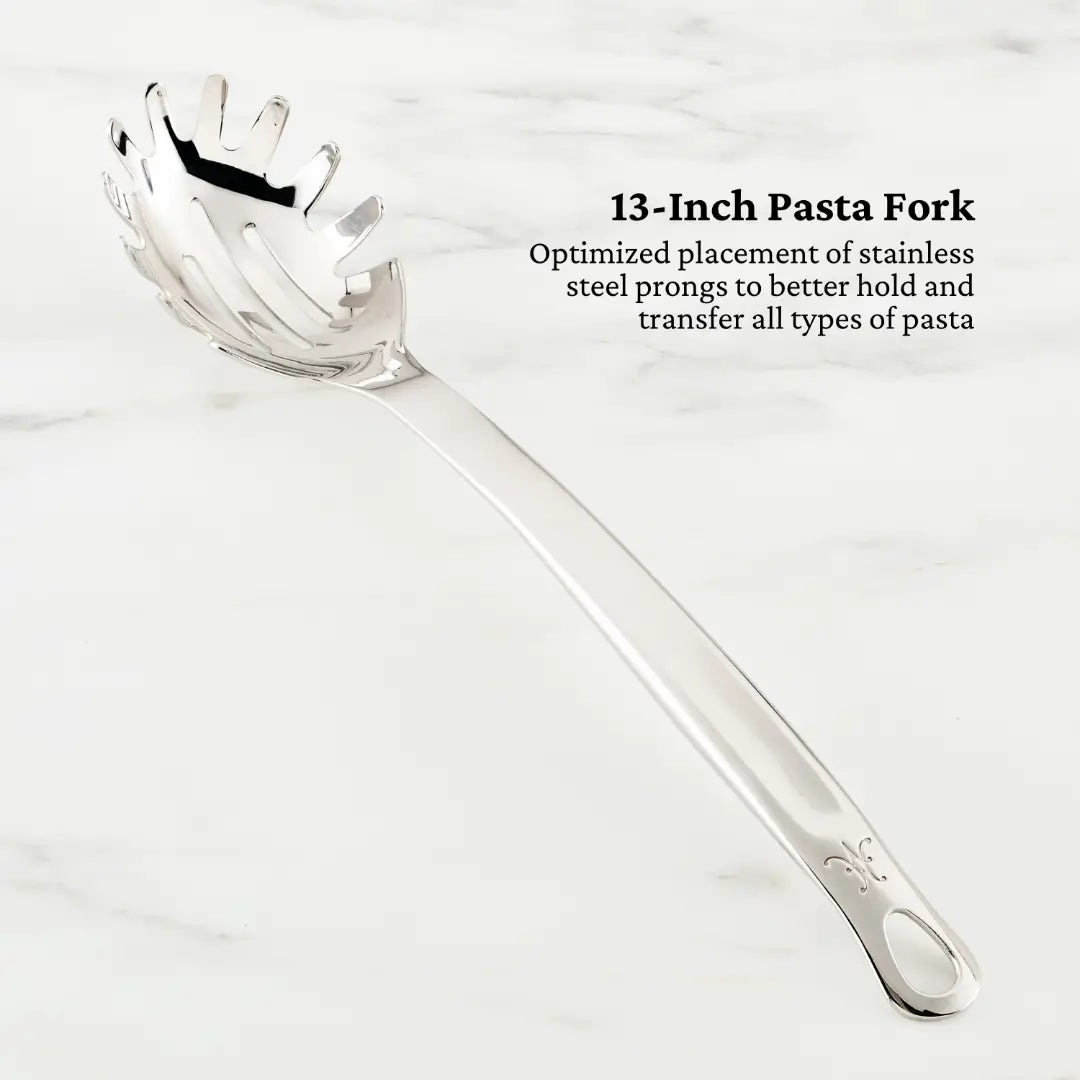 A 13-inch stainless steel pasta fork from the Hestan Provisions Deluxe Chefs Tool Set is displayed on marble. Its design, perfect for transferring pasta, features finely optimized prongs for performance and is highlighted as essential among chefs tools.