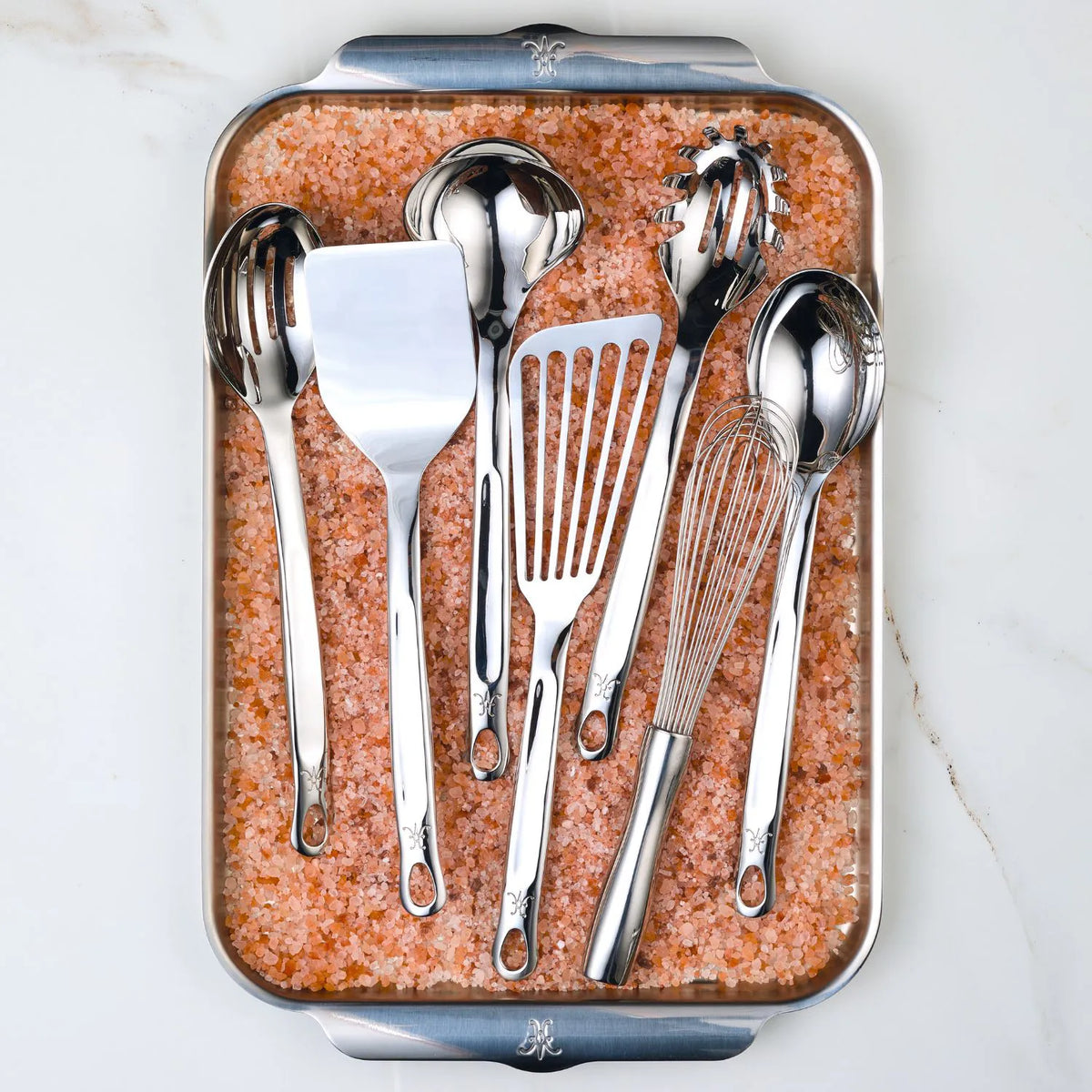 The 8-piece Ultimate Chefs Tool Set by Hestan Provisions, made of 18/10 stainless steel, features spoons, spatulas, and a whisk elegantly displayed on pink Himalayan salt in a rectangular tray. Ideal for both Michelin-starred chefs and home cooks seeking premium kitchen utensils.