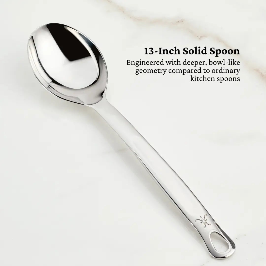 A shiny, silver 13-inch solid spoon made from 18/10 stainless steel with a deep design rests on a light surface. Text beside it reads, Part of Hestan Provisions: Ultimate Chefs Tool Set, 8-piece. Engineered with a deeper bowl-like geometry compared to ordinary kitchen spoons.