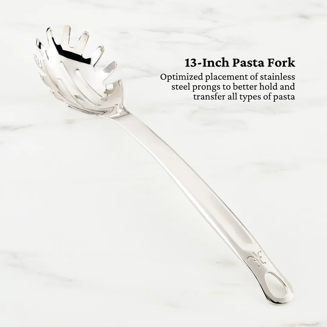 On a white marble surface: a 13-Inch Pasta Fork from the Ultimate Chefs Tool Set by Hestan Provisions, crafted with 18/10 stainless steel and optimized prong placement for holding and transferring all pasta types.