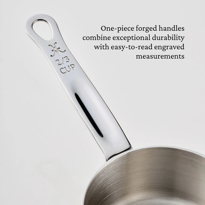 A stainless steel measuring cup from the Hestan Provisions® Odd-Size Measuring Cups Set, 3-Piece features a shiny, one-piece handle engraved with 2/3 CUP. Text next to the handle highlights its durability and the easy-to-read engraved measurement. This essential piece is part of the Hestan Provisions® stainless steel measuring cup set, designed for precision and lasting performance in any kitchen.
