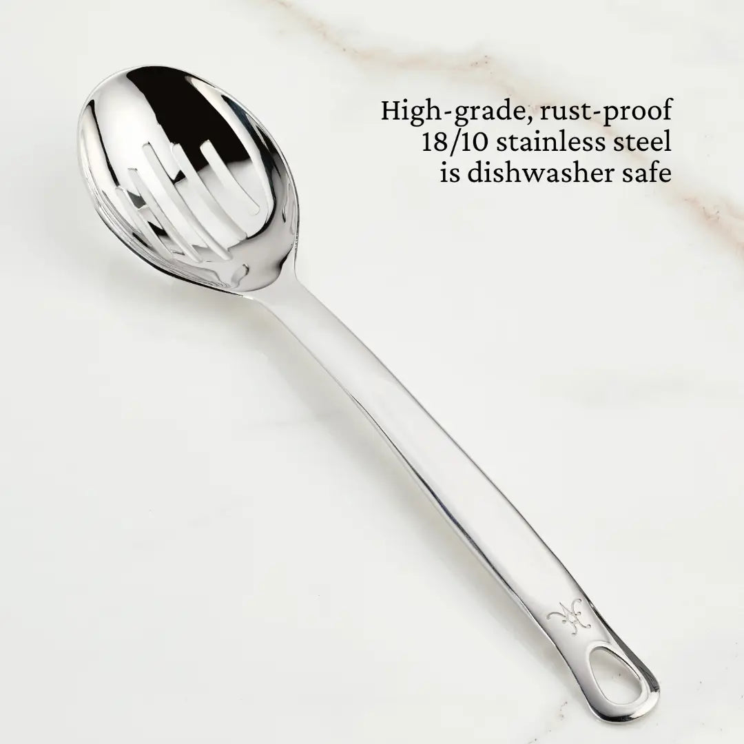 A shiny Deep Slotted Spoon, 13-inch from the Hestan Provisions Chefs Tools collection, crafted with rust-proof 18/10 stainless steel, is displayed on a smooth, light surface. Beside it, text indicates the spoon is dishwasher safe.